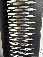 Close-up image showing the black metal mesh grate surface with pattern of elongated oval cutouts for traction and drainage.