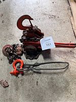 Ratchet lever puller with chain and handle, and wire rope sling with red shackle on concrete floor