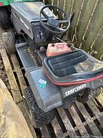 Front-left angled view of the Craftsman riding lawn mower showing the seat with a red fuel container, steering wheel, tires, and side decals.