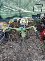 Front view of the green Briggs & Stratton MTD 26-inch rotary tiller showing handles, engine, and wheels on outdoor ground with leaves.