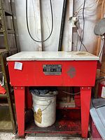 Front view of red and white Burgess Safety Parts Cleaner model B-10, showing label and bucket beneath.