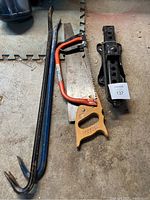 Photo shows two metal crowbars, a Mastercraft bowsaw with an orange handle, a large handsaw with a wooden handle, and a black metal car jack