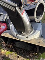 Close-up of the snow blower discharge chute showing black plastic chute and metal base plate with warning label.