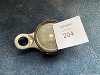 Smiths brand motorcycle speedometer lying on blue carpet, showing side mounting bracket and dial face with mph markings up to 150.