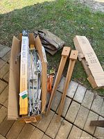 Box containing large quantity of metal stakes, cables, packaging, and two rust-colored metal fence post supports.