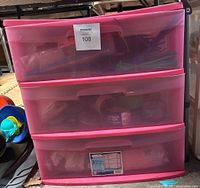 Full view of the three-drawer pink plastic storage bin containing items inside drawers.