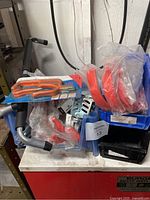 Overview of assorted red metal hooks in plastic packaging, caster wheels, locks, and black storage organizers on a shelf.