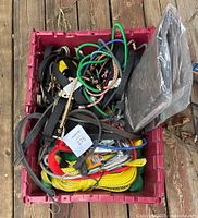 Crate filled with assorted straps, ratchet straps, bungee cords, wire ropes, and a green poly tarp.