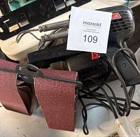 Weller D550 soldering tool with two metal soldering tips, Craftsman belt sander, and hanging sanding belts shown on a table.