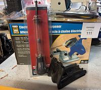 Full lot view showing electric chain saw sharpener with box, packaged screwdriver, and mechanic's stethoscope in packaging