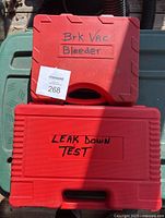 Two red tool cases stacked outdoors; top case labeled 'Brk Vac Bleeder,' bottom case labeled 'Leak Down Test'