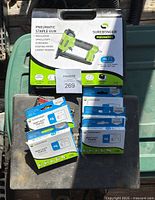 Photo showing Surebonder pneumatic staple gun box and multiple boxes of Surebonder heavy duty staples on a dark surface.