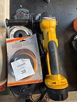 Photo showing Dewalt DC411 cordless angle grinder with side handle and multiple sanding discs including flap discs.