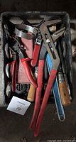 Top view of toolbox with assorted hand tools including pliers, adjustable wrench, strap wrench, pipe wrench, and other tools