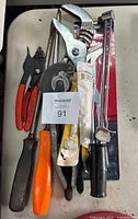Photo showing a variety of hand tools including pliers with orange handles, an adjustable pipe wrench, flat head screwdrivers with black and orange handles, and torque wrench