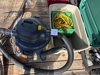 Photo showing Mastervac shop vacuum with large beige plastic storage bin containing extension cord and crate.