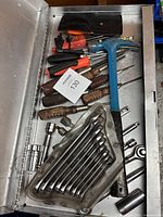 Top view of assorted screwdrivers, combination wrenches, sockets, and ratchets inside metal toolbox drawer.
