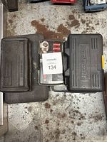 Top view photo showing three black plastic cases containing tool sets on a workbench with some rust stains.