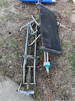 Metal motorcycle girder forks with coil spring suspension lying on ground outdoors with an AC condenser radiator set beside them.
