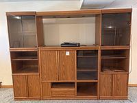 Full front view of the three-piece wood entertainment center showing storage cabinets, glass doors, and shelving spaces with centered space for electronics.