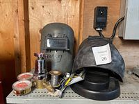Photo showing welding helmets, gas regulator parts, welding wire spool, flint strikers, red capped containers, and other welding accessories on a shelf.