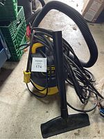 Stanley yellow and black wet/dry vacuum with attached hose, extension cord wrapped around it with yellow plug, placed on a concrete floor.