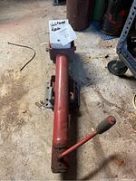 Red wheel trailer jack shown on floor with crank handle and wheel attachment.