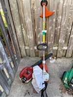 Homelite gas-powered leaf blower and weed wacker combo unit leaning against a wooden fence with collection bag attached