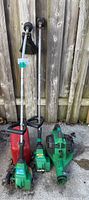 Two Featherlite yard tools and a red gas can positioned upright on concrete ground in front of a wooden fence.