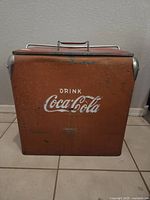 Front view showing orange body with white 'Drink Coca-Cola' logo and metal corner protectors.