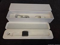 Full view of the Apple Watch Sport in white band with charging cable and adapter in original packaging box.
