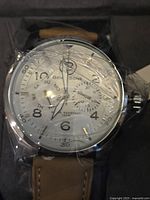 Close-up of the watch face showing white dial with numbered markers, subdials, and brown leather strap.