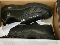 Pair of black K-Swiss leather sneakers in box with visible K-Swiss branding and tissue paper inside, box shows wear