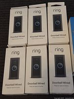 Seven boxes of Ring Wired Doorbells arranged flat showing front packaging with a black doorbell and blue ring button.