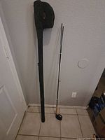 Full length view of fly fishing rod with black protective carrying case standing against a wall.