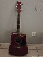 Full front view of the Hohner acoustic electric guitar in red wine color with cutaway body standing against wall