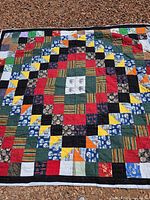 Full view of the handmade multicolor patchwork quilt laid flat on the ground, showcasing its central diamond pattern with various fabric squares and triangle accents.