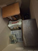 Overhead view of cardboard box containing wooden jewelry boxes and metal tin