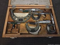 Top view of vintage metal micrometers fitted in a wooden case, showing multiple sizes and styles including Mitutoyo brand.