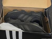 Photo showing the pair of black Adidas athletic shoes inside an open original box, shoes appear new and unworn.