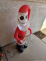 Front view of an inflatable Jack Skellington dressed in red Santa costume, standing outdoors against a wall.