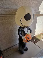 Front-left view of the Jack Skellington inflatable holding a pumpkin, showing large head and pinstripe suit.