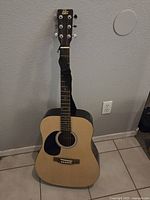 Full frontal photo of the Rogue acoustic guitar showing the body, neck, and headstock, placed upright against a wall.