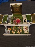 Full view of white jewelry box opened showing assorted vintage jewelry inside compartments and drawer.