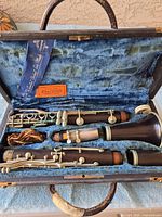 Open clarinet case showing three-piece clarinet inside with blue plush lining and metal keys showing tarnish and discoloration.