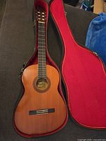 Full view of vintage Yamaha acoustic guitar open in red-lined case showing natural wood body and nylon strings
