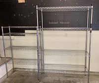 Both metal wire shelving units shown side by side against black pegboard wall and concrete floor, smaller shelf on left, larger on right.