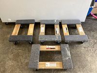 Top view of four movers dollies arranged on a concrete floor, showing carpet padding and casters.