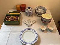 Blue and white plates, multi-patterned colorful bowls, ceramic jar, terra cotta tea set in box and small measuring cups on table