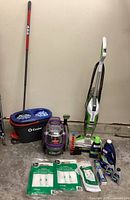 Full lot view showing Bissell SpotClean Pet Pro, Bissell upright cleaner, O-Cedar mop and bucket, cleaning products and vacuum bags